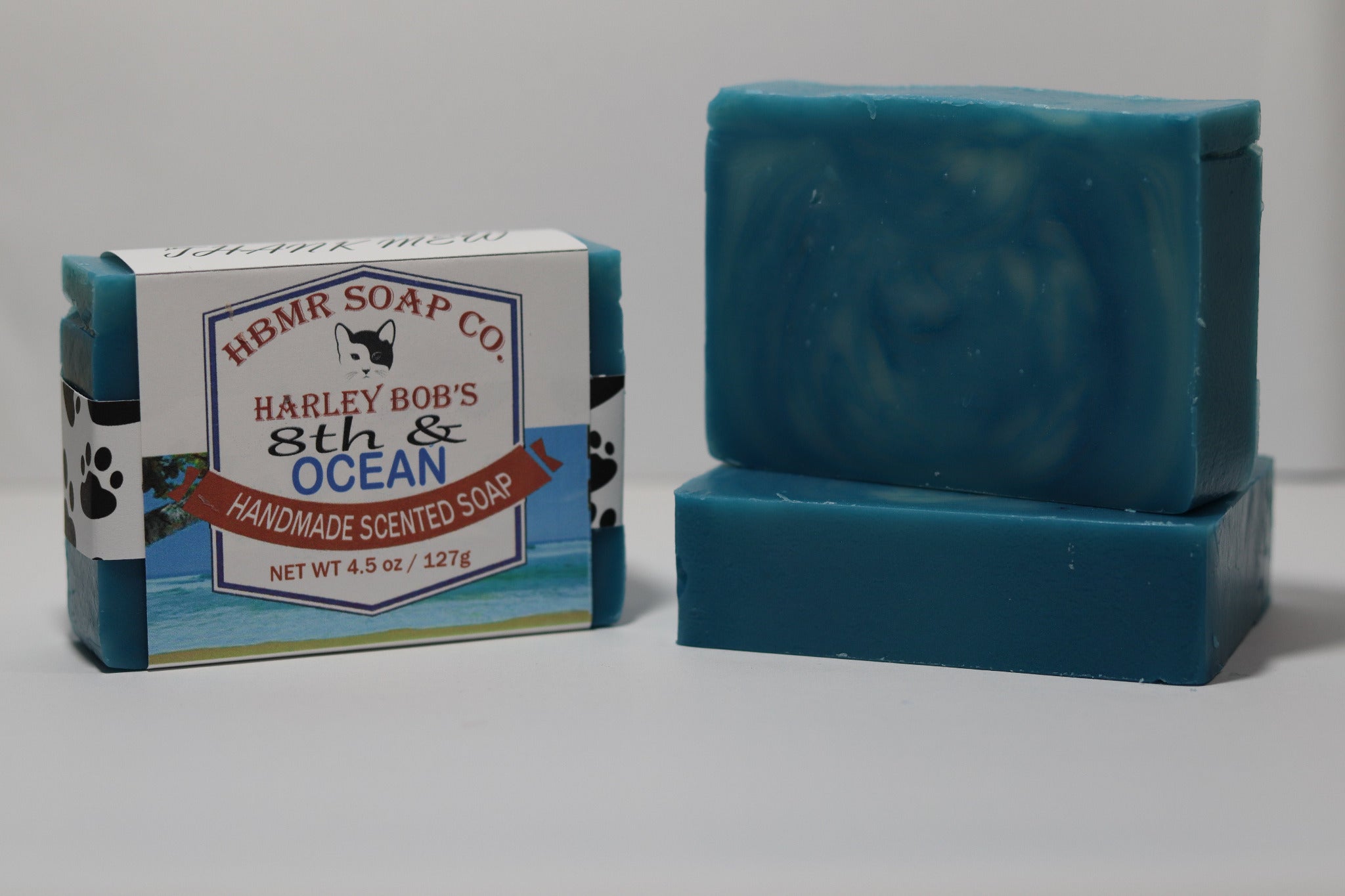 Two bars of blue soap and its packaging with 'Harley Bob's 8th & Ocean' branding on a gray background.