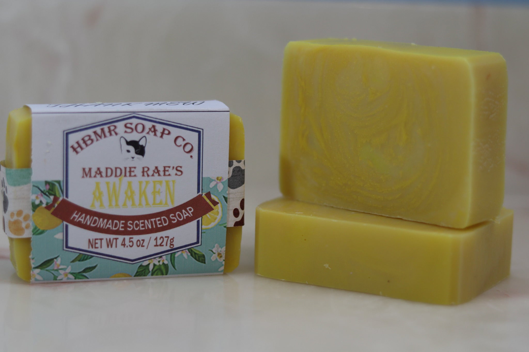 Yellow soap bar with packaging labeled 'HBMR Soap Co. Maddie Rae's Awaken' on a light background
