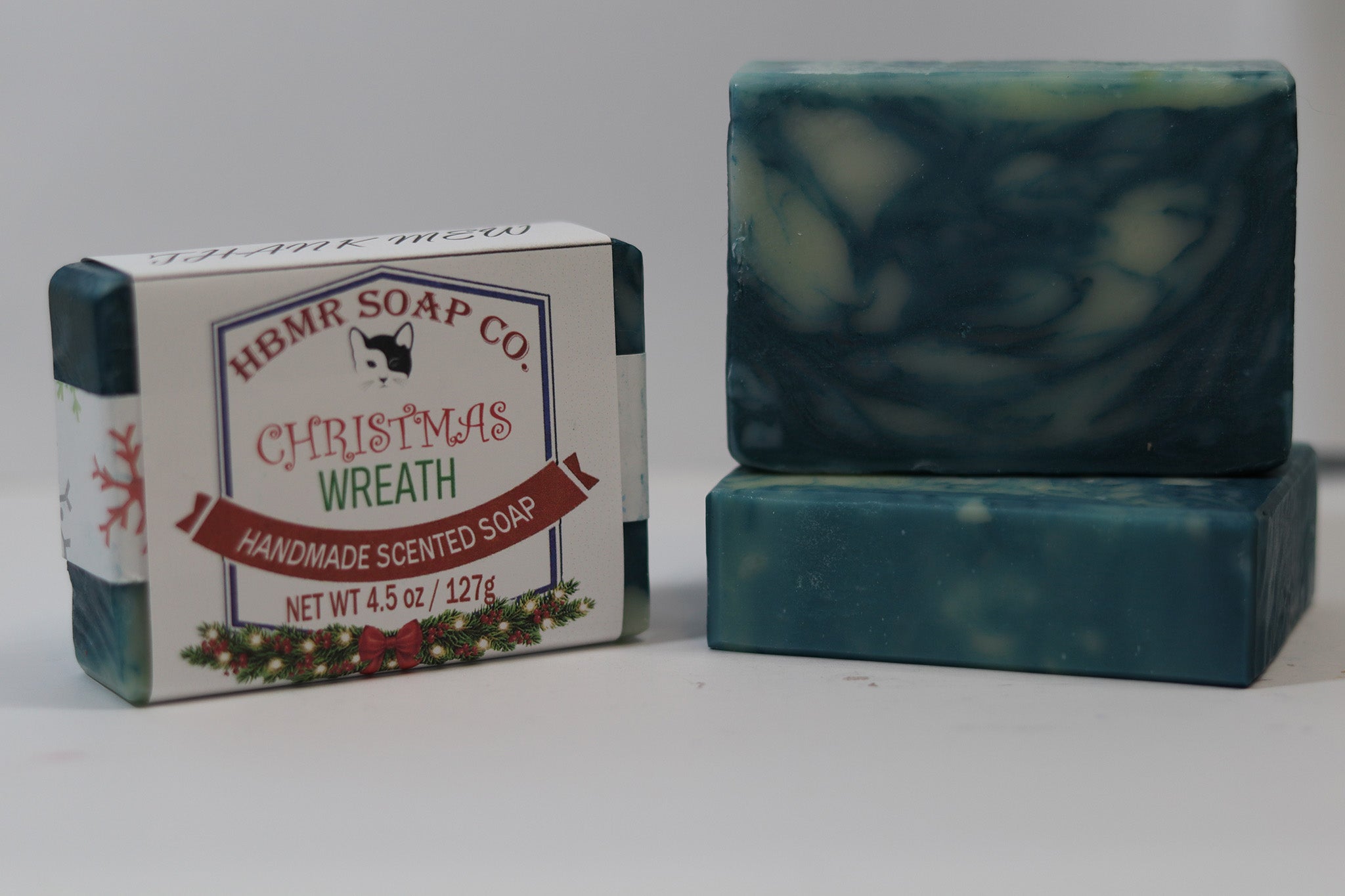 Two bars of soap with a HBMR Soap Co. Christmas Wreath packaging on a white background
