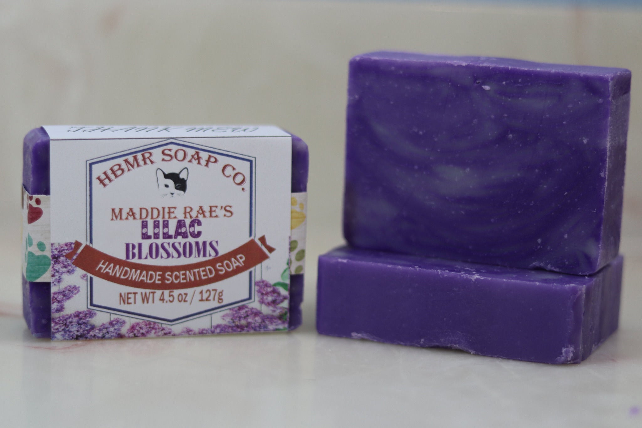 Purple soap bar with packaging labeled 'HBMR Soap Co. Maddie Rae's Lilac Blossoms' on a white background